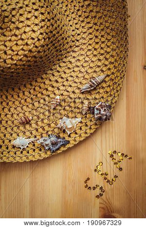 Straw Hat with seashells in wooden background