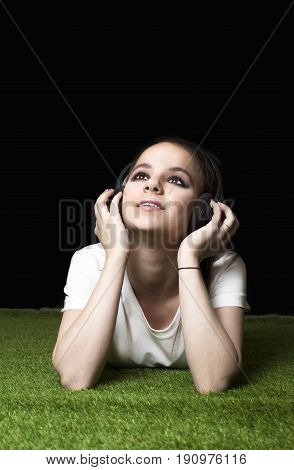 Attractive girl listening to music streaming with headphones at nigt on a meadow. Black background