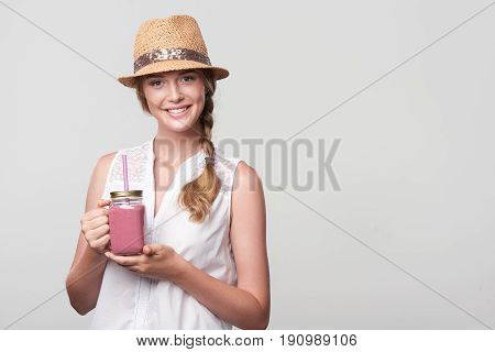 Smiling girl holding jar tumbler mug with pink smoothie drink, portrait over grey background with blank copy space