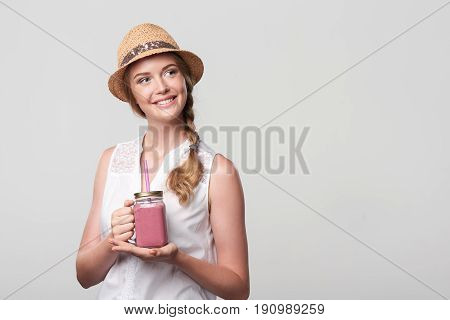 Smiling girl holding jar tumbler mug with pink smoothie drink, looking at blank copy space