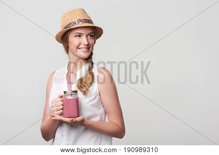 Smiling girl holding jar tumbler mug with pink smoothie drink, looking at blank copy space