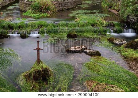 Long Exposure Of The River Flowing Past A Sword Sticking Out Of The River In  Cheddar Village In Som