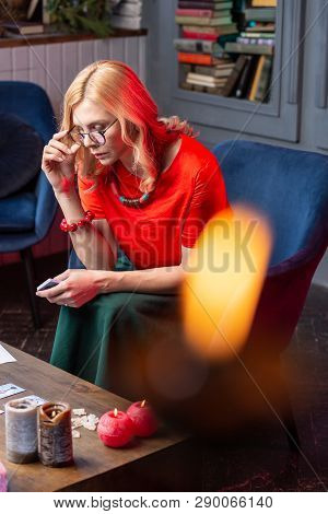 Female Blonde Astrologist Sitting At The Table With Burning Candles