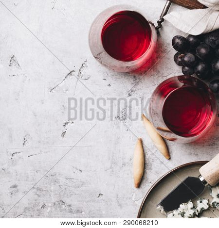 Glasses of red wine, cheese and grapes on rustic concrete background