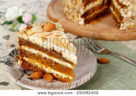 Close-up The Slice  Of Vegetarian Carrot Cake With Almonds On A Saucer And A Fork Near. Wooden Board