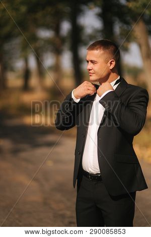 Young Man Walking In The Park. Handsome Groom In Black Suit