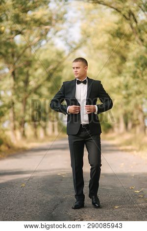 Young Man Walking In The Park. Handsome Groom In Black Suit