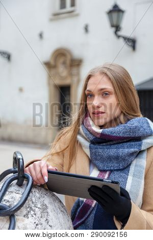 Blonde Beautiful Woman Holding Tablet On City Street. Portrait Of Young Woman Wearing Tartan Scarf S