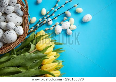 Holiday contept decoration with easter eggs and yellow tulips over blue background. Top view with copy space.