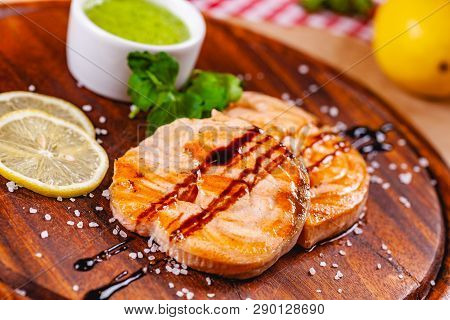 Grilled Fish Steak Served With Sauce And Lemon On Wooden Cutting Board. Close Up