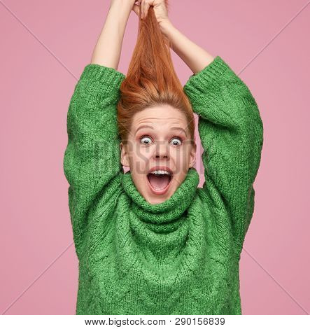 Bright Young Redhead Girl In Green Sweater Pulling Hair Up And Looking Amazed At Camera