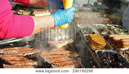 Chef With Blue Gloves And Cooked Sausages In The Kiosk Of Street Food