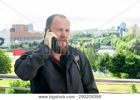 Business Mature Male Tourist With A Beard Talking On The Phone And Make An Appointment On The Backgr