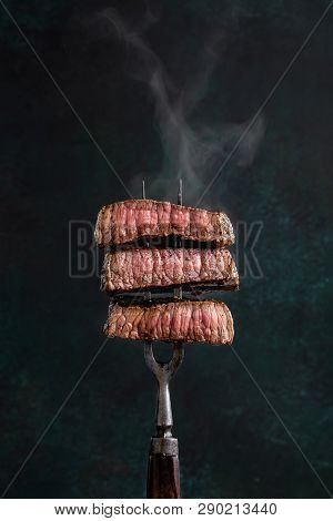 Slices Of Beef Steak With Steam On Vintage Fork On Dark Background