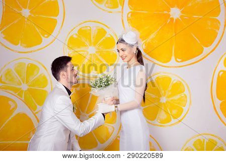 Happy Man In Knees In Front Of Charming Bride With Bouquet Looking At Each Other In Love Against Ora