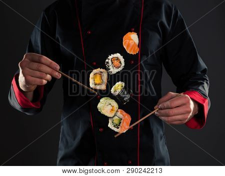 Closeup of master chef holding wooden chopsticks with flying sushi pieces. Concept of food preparation, ready for product placement.