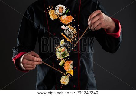 Closeup of master chef holding wooden chopsticks with flying sushi pieces. Concept of food preparation, ready for product placement.