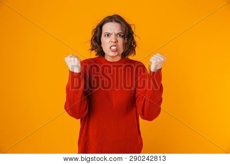 Portrait of uptight woman 20s wearing sweater gesturing and yelling while standing isolated over yellow background