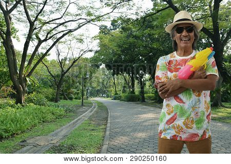 Happy Elderly Traveler Asian Man Wearing Summer Shirt, Straw Hat And Sunglasses Holding Colorful Wat