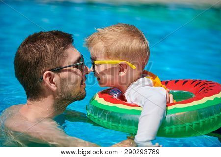 Three year old toddler boy in resort swimming pool eskimo kissing his father. Summer family vacation at Maldives.