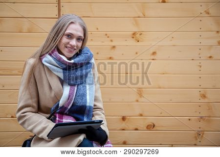Blonde Beautiful Woman Holding Tablet Outdoor. Portrait Of Young Woman Wearing Tartan Scarf In Front