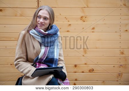 Blonde Beautiful Woman Holding Tablet Outdoor. Portrait Of Young Woman Wearing Tartan Scarf In Front