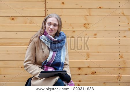 Blonde Beautiful Woman Holding Tablet Outdoor. Portrait Of Young Woman Wearing Tartan Scarf In Front