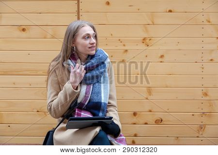 Blonde Beautiful Woman Holding Tablet Outdoor. Portrait Of Young Woman Wearing Tartan Scarf In Front