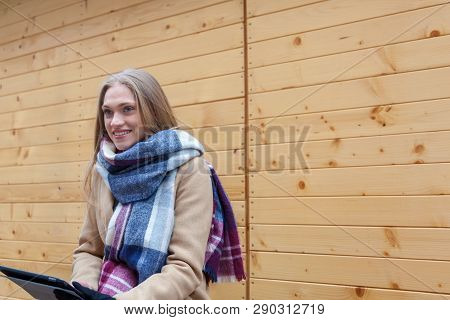 Blonde Beautiful Woman Holding Tablet Outdoor. Portrait Of Young Woman Wearing Tartan Scarf In Front