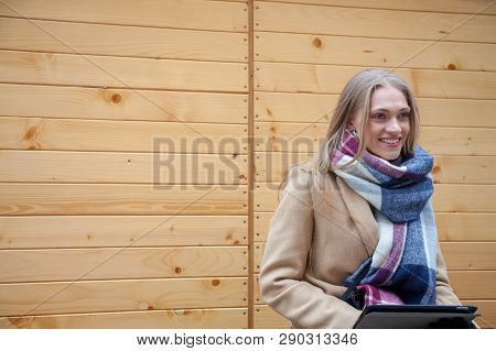 Blonde Beautiful Woman Holding Tablet Outdoor. Portrait Of Young Woman Wearing Tartan Scarf In Front