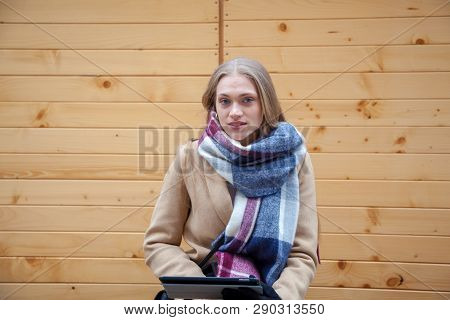 Blonde Beautiful Woman Holding Tablet Outdoor. Portrait Of Young Woman Wearing Tartan Scarf In Front