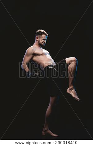Muscular Barefoot Strenuous Boxer In Boxing Gloves Doing Kick Isolated On Black