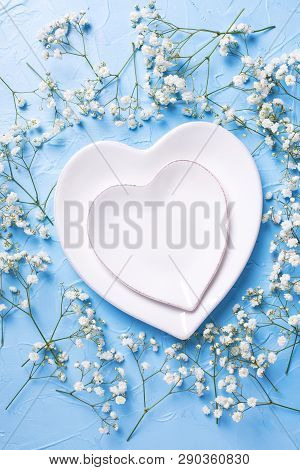 Plates In Form Of Hearts And  Fresh White Gypsofila  Flowers On Blue Textured Background. Top View. 