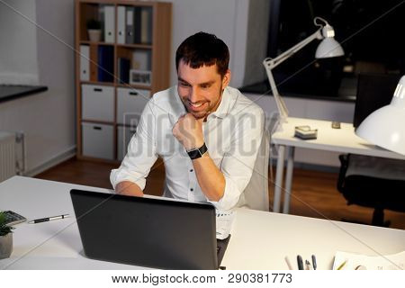 business, deadline and people concept - businessman with laptop computer working at night office