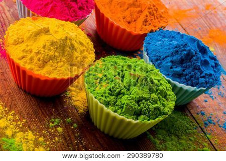 Colorful Holi powder in cups closeup. Bright colours for Indian holi festival in clay pots. Selective focus. Black background, top view