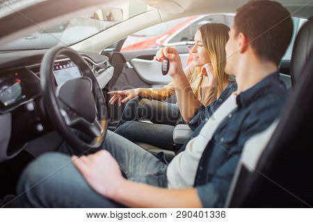 Young Family Buying First Electric Car In The Showroom. Attractive Man Behind Steering Wheel Holding