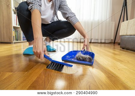 Detail Of Female Hands Holding A Broom And Sweeping Floor, Collecting Dust Onto A Dustpan
