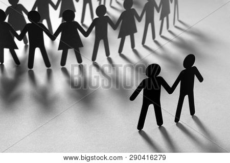Black paper figure of male couple in front of a crowd of paper people holding hands on orange surface. Social movement, protest, minorities concept.