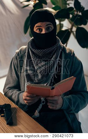 Shocked Terrorist In Black Mask Reading Book At Table