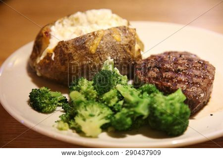 Steak and Potato dinner. Steak, Potato, Broccoli with cheese dinner on a white plate in a restaurant.  Dinner time

