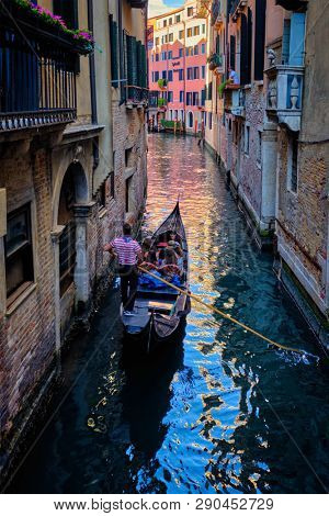 VENICE, ITALY - JUNE 27, 2018: Narrow canal between colorful old houses with gondola boat with tourists and gonolier in Venice, Italy