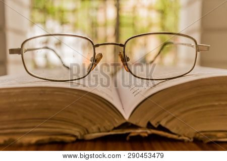 An Open Book And A Eyeglass Nicely Placed On Wooden Table On A Warm Sunny Morning, Side View Close U