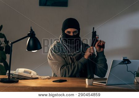 Criminal In Black Mask Looking At Camera And Loading Gun In Room