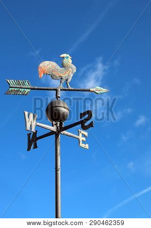 Old Wind Vane With Cock On Top And Cardinal Points On The Blue Sky