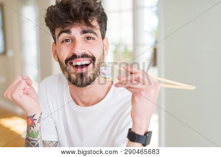Young man eating asian sushi using chopsticks screaming proud and celebrating victory and success very excited, cheering emotion