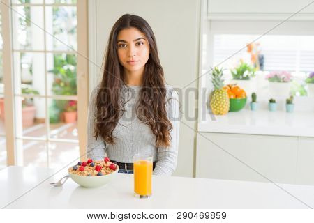 Young woman eating healthy breakfast in the morning with serious expression on face. Simple and natural looking at the camera.
