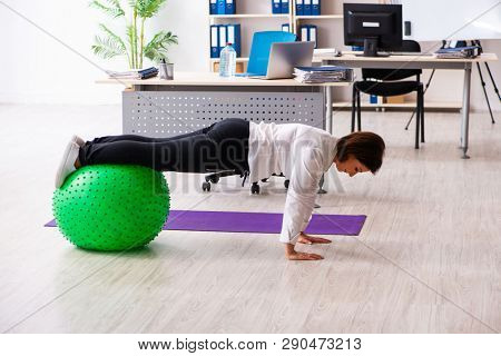 Middle-aged female employee doing exercises in the office 
