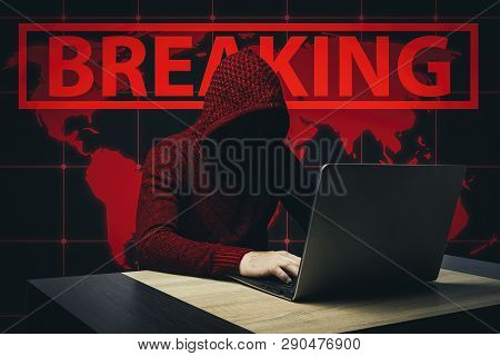 Faceless Man In A Hooded Robe Sits At A Table With A Laptop. Concept Of Hacking And Stealing User Da