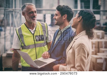 Warehouse managers and worker discussing with laptop in warehouse office