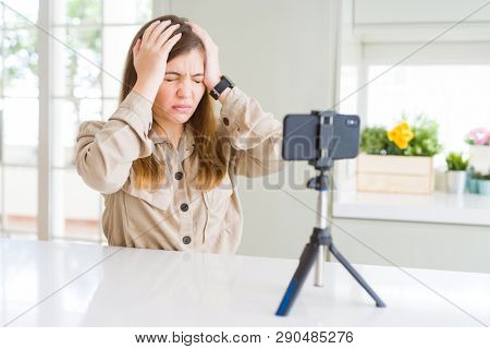 Beautiful young woman doing online video call using smartphone webcam suffering from headache desperate and stressed because pain and migraine. Hands on head.